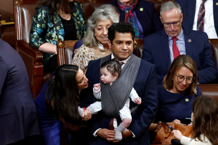 Rep. Alexandria Ocasio-Cortez, holds Rep. Jimmy Gomez's baby's foot.