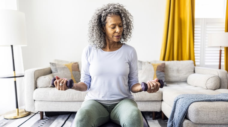 Senior woman lifting weights in living room.