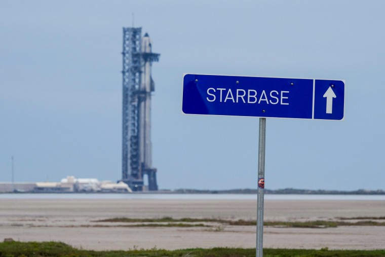 A sign that says "Starbase" with an arrow pointing up, stands in front of a rocketship in the distance