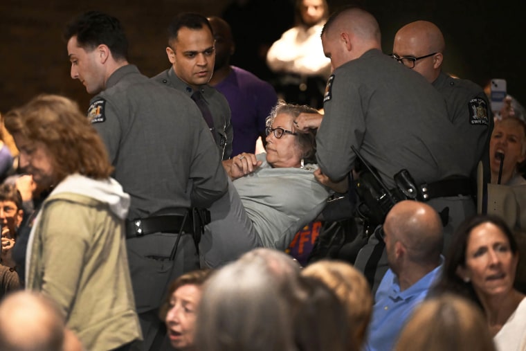 A woman is carried out by law enforcement at a town hall