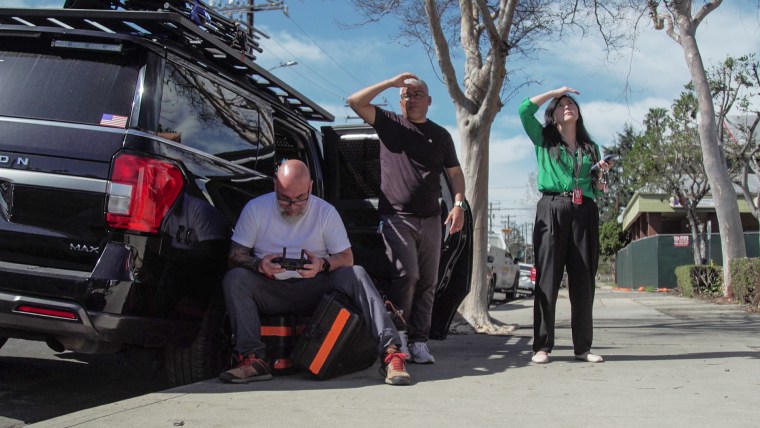 Three people outside on a sidewalk next to a car