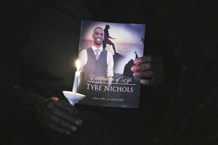A man holding a candle and a photo of Nichols.