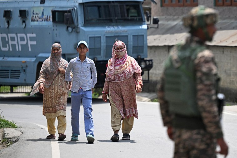 Indian security personnel stand guard as people walk along a road in Wuyan near Srinagar.