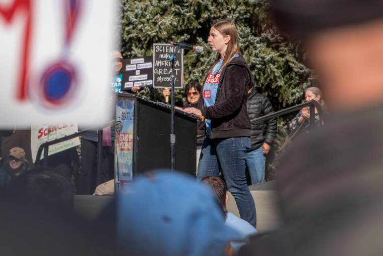 Kristin Weinstein speaks at a podium outside amongst a large crowd