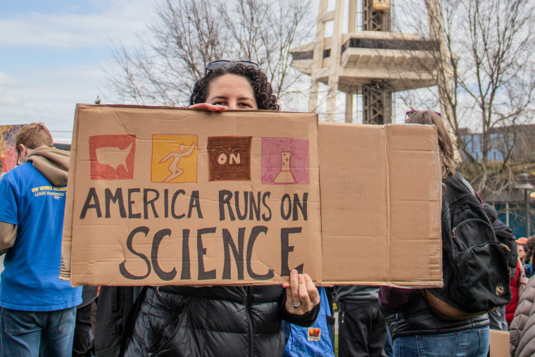 A person holds a cardboard sign that says "America runs on science"