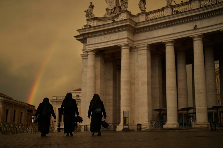 Nuns walk along St. Peter's Square as a rainbow forms