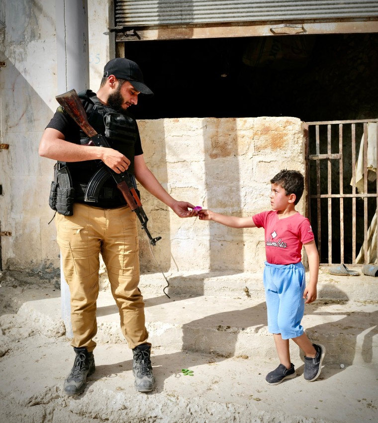 A member of the Syrian Hayat Tahrir al-Sham forces, a rebel group who have formed an interim government after the fall of Assad, accepts a gift from a young boy in Dabiq on Friday.