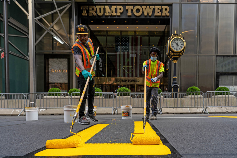 Two people painting a yellow 'Black Lives Matter' mural on Fifth Avenue directly in front of Trump Tower in New York