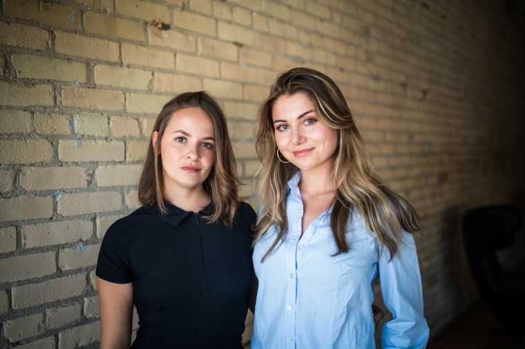 Lea Burbidge Izquierdo, left, and Francesca Albo stand next to each other in front of a beige brick wall