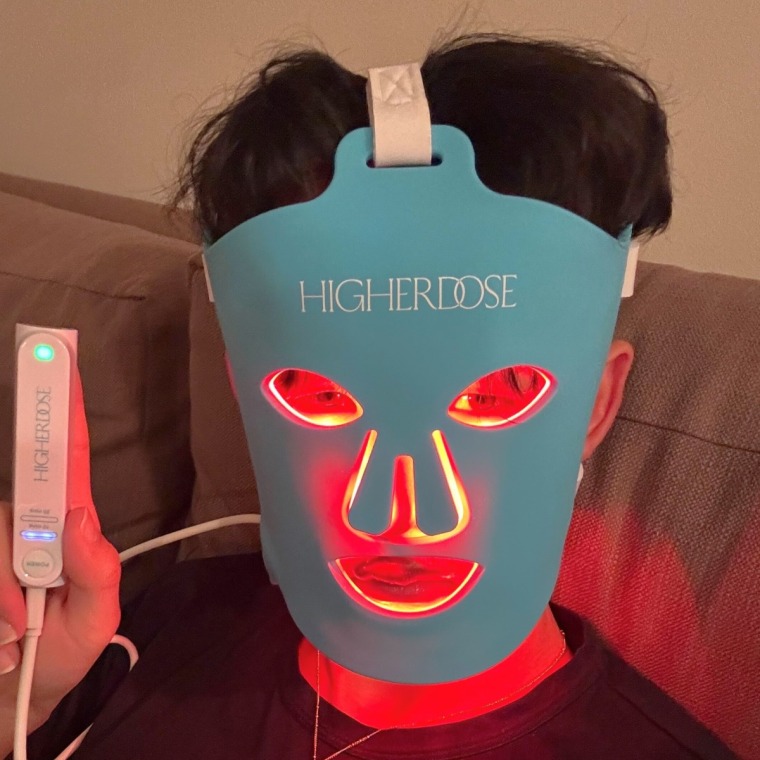 A man wearing the HigherDose red light face mask holding up the controller.