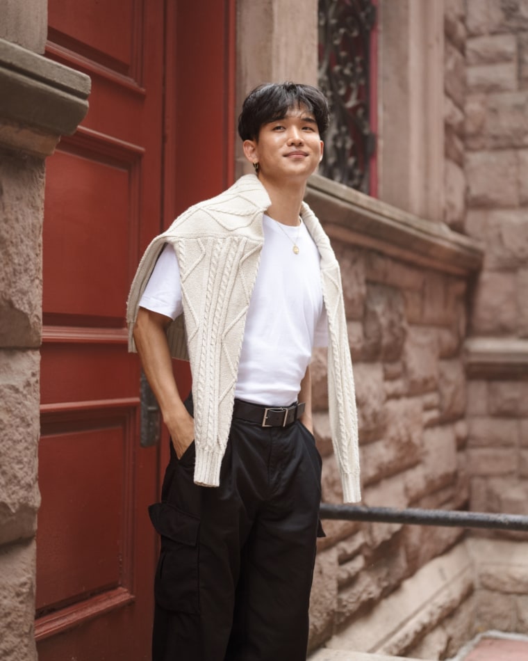 A model wearing a Abercrombie & Fitch white t-shirt tucked into black trousers, with a cream colored sweater thrown over their shoulders