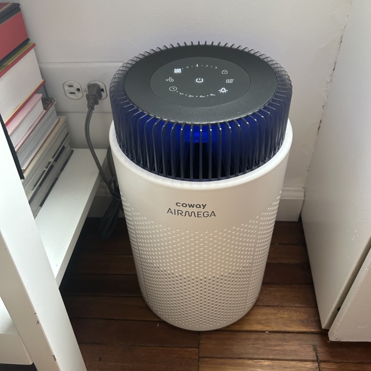 A photo of the Coway Airmega 100 air purifier plugged into the corner of a room.