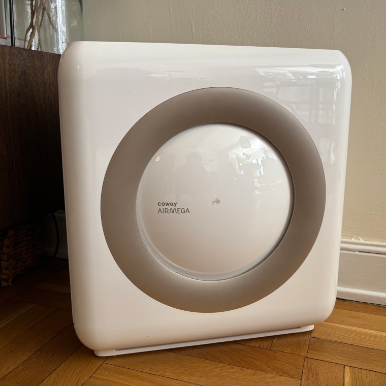 A photo of the Coway Airmega AP-1512HH Mighty air purifier plugged into the corner of a room with hardwood flooring and a white wall.