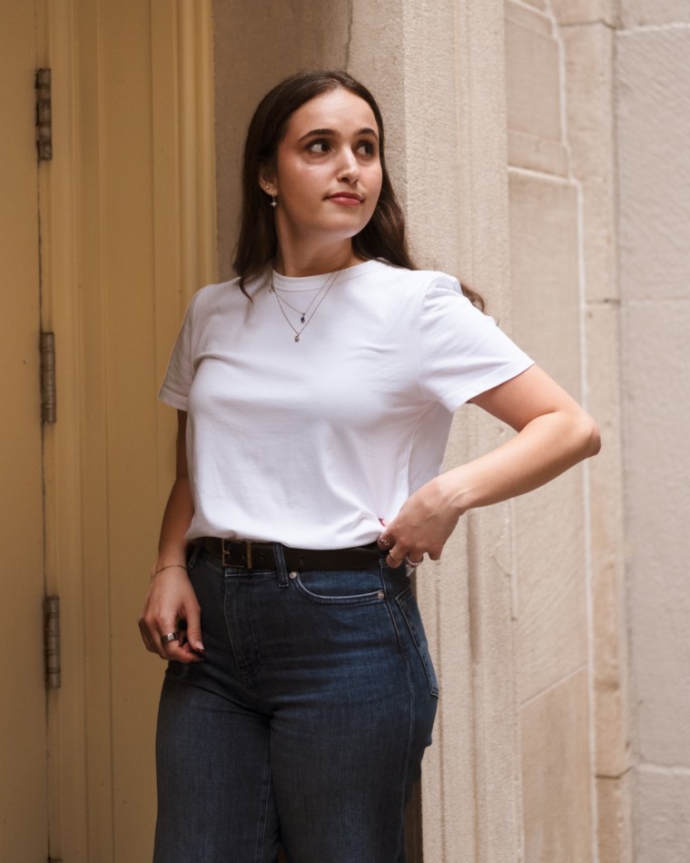 A model stands under an arch while wearing a white t-shirt from Madewell and dark wash denim.