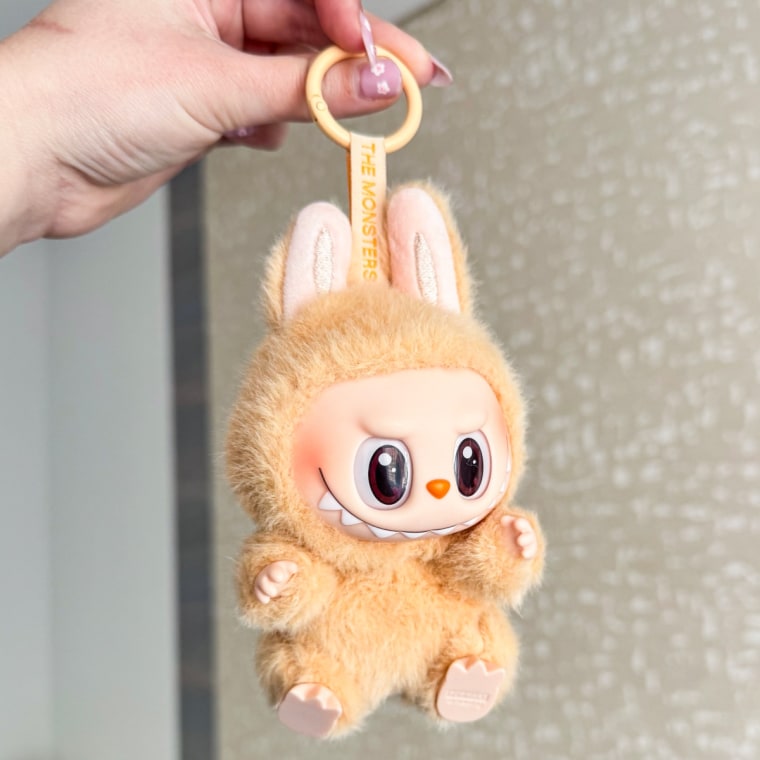 Light brown Labubu with brown eyes being held up by hand.
