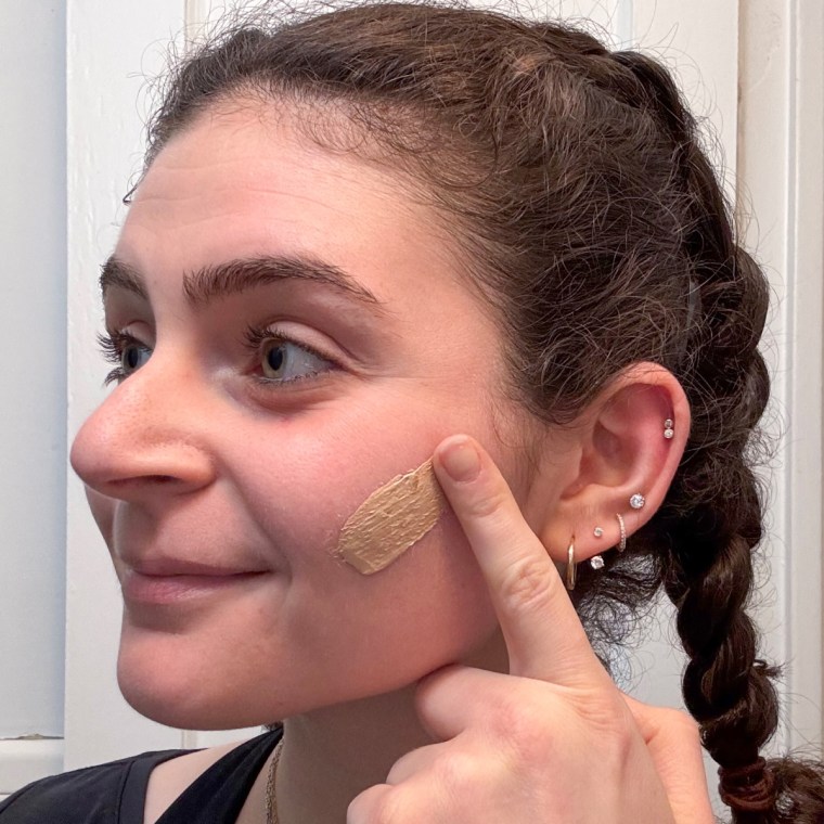 A woman applying Naturium’s Dew-Glow Tinted Moisturizer SPF 50+.