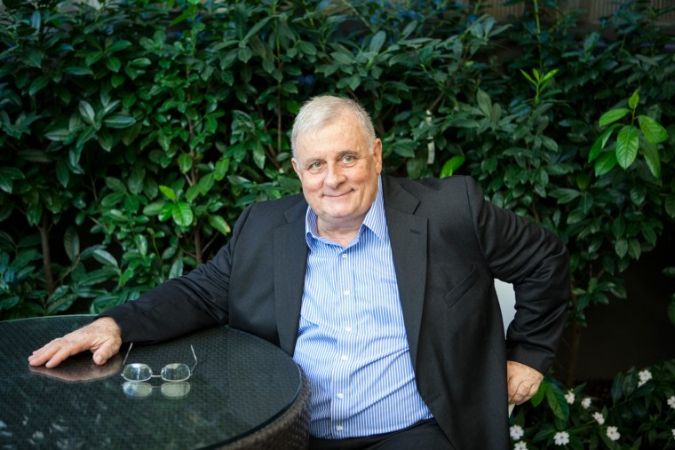 Edmund White sits at a table outside in front of greenery
