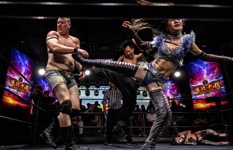 Wrestlers Yuki Kamifuku and Chen Wenbin kicking opponent Big Sam during their tag team match.