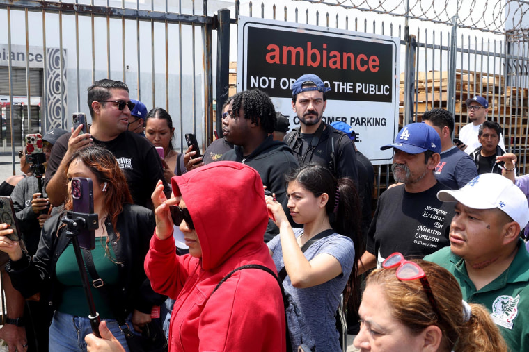 People gather in front of Ambiance Apparel after several employees were taken into custody by federal agents