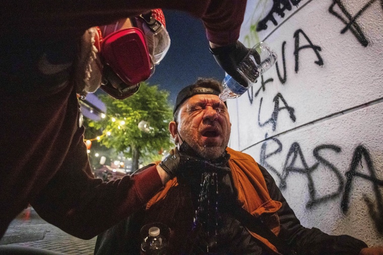 An injured protester is helped by another pouring water into their eyes
