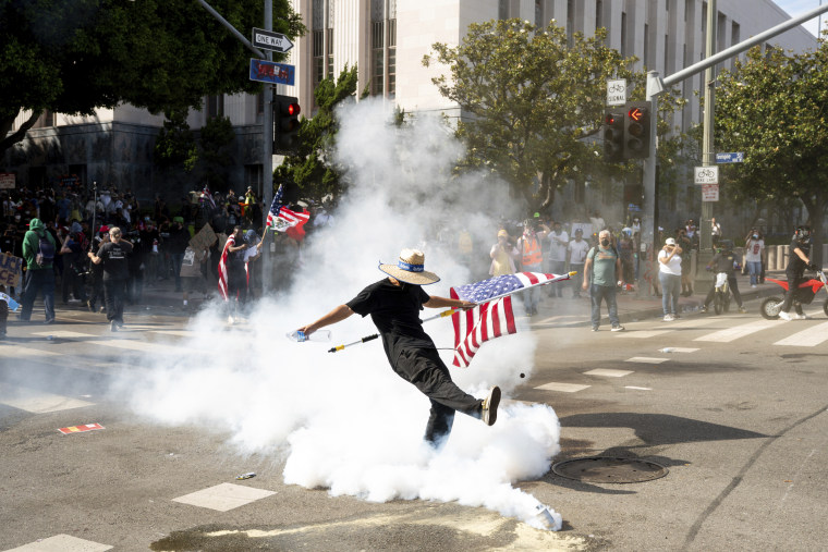 A protester holding an American flag kicks a tear gas canister.