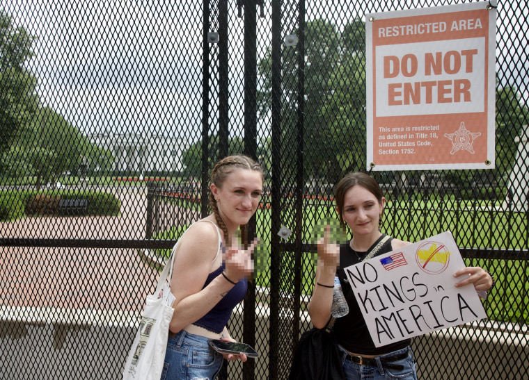 Image: Two protesters holding signs and flashing the middle finger in front of the White House.
