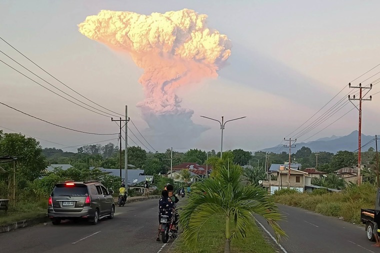 People watch from a distant road as Mount Lewotobi Laki-Laki spews volcanic materials into the air