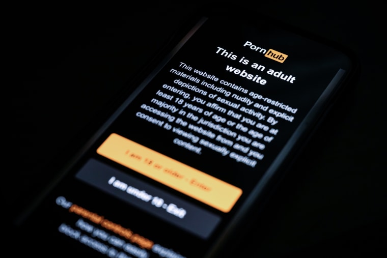 The age-restriction warning screen of the website PornHub is displayed on a digital phone screen