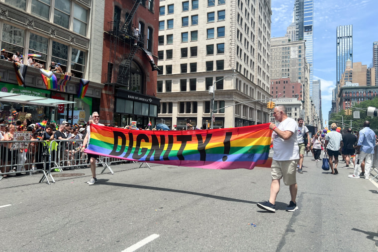 People march with a rainbow sign that says "Dignity"