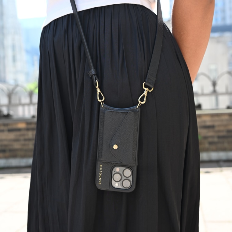 A close up of a woman wearing a Bandolier Hailer phone case, which hangs against her black skirt.