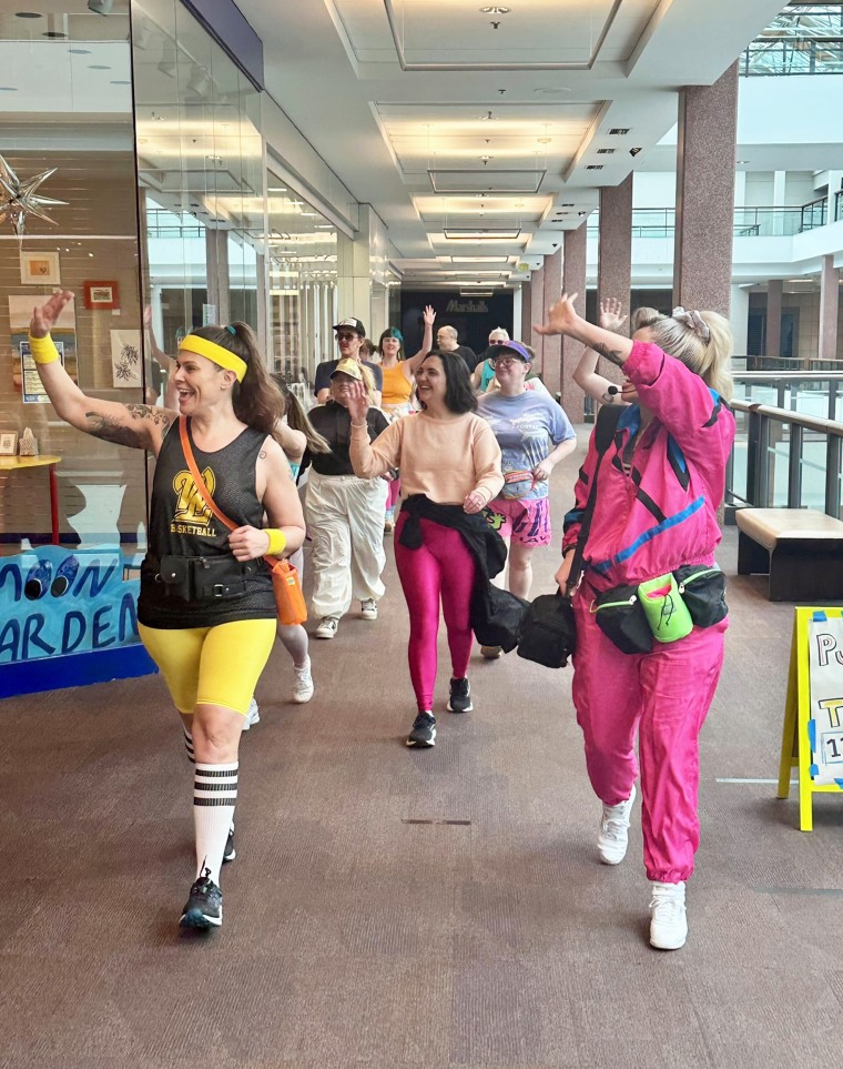 Krista Catwood (R) and her group of mall-walkers called “Food Court 5000” wave to shoppers.