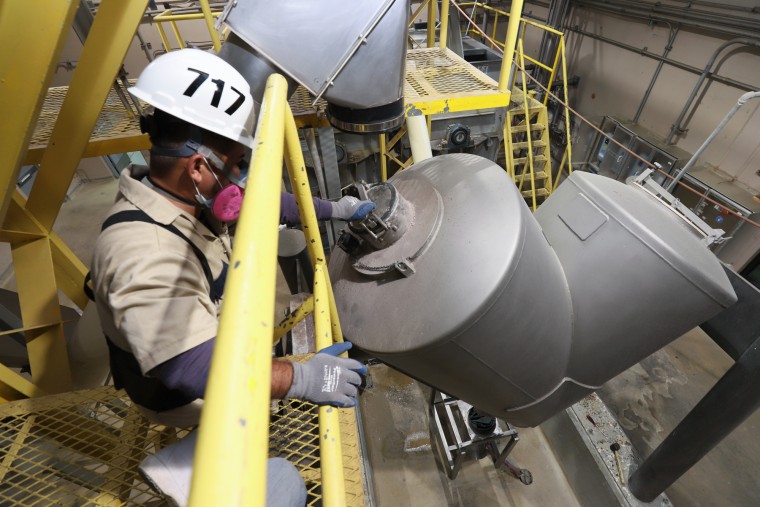 A worker uses a machine to mix food inside of a factory