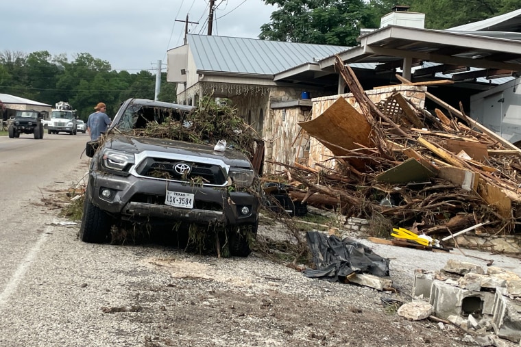 Heavy debris that slammed up against one side of a home, a damaged car is parked outside on the street
