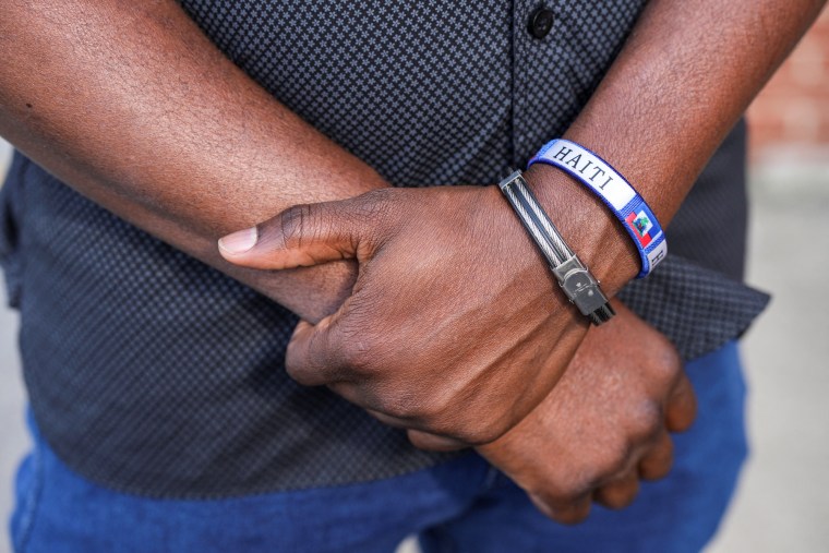 Two arms crossed over one another, a bracelet with the text "Haiti" on it is worn on his wrist