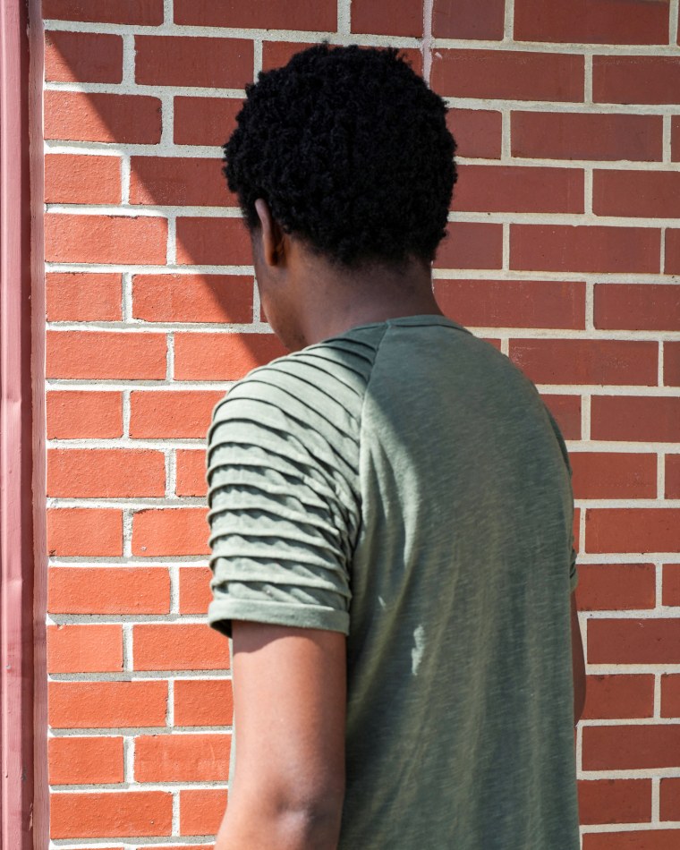 I.M. has his back to the camera, posed against a brick wall