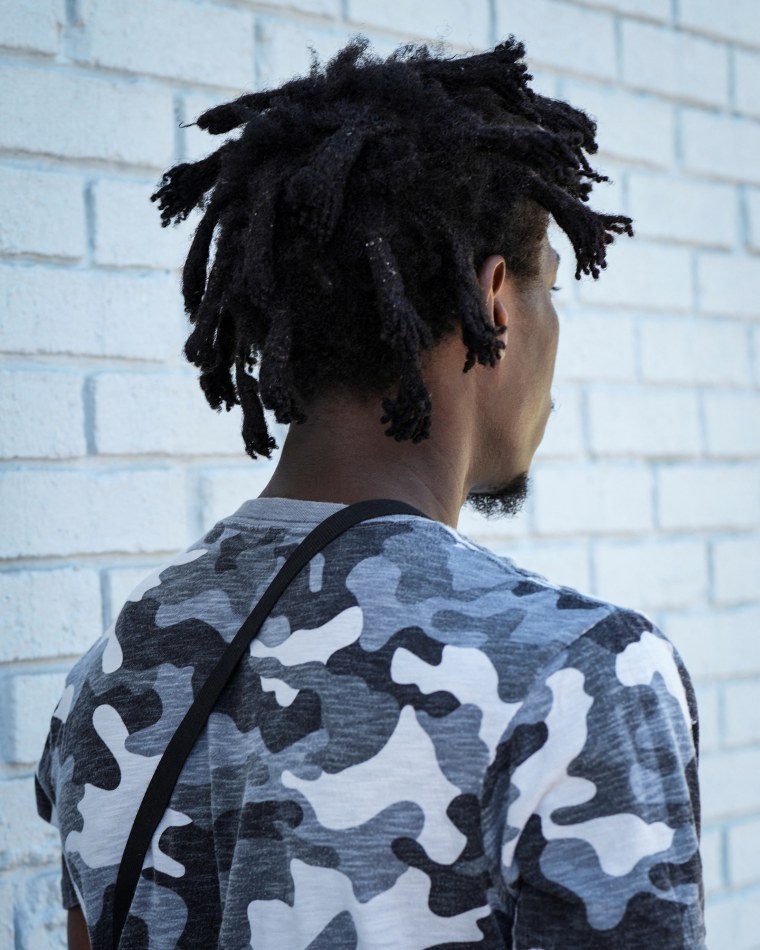 Jean, back to the camera, stands against a white brick wall