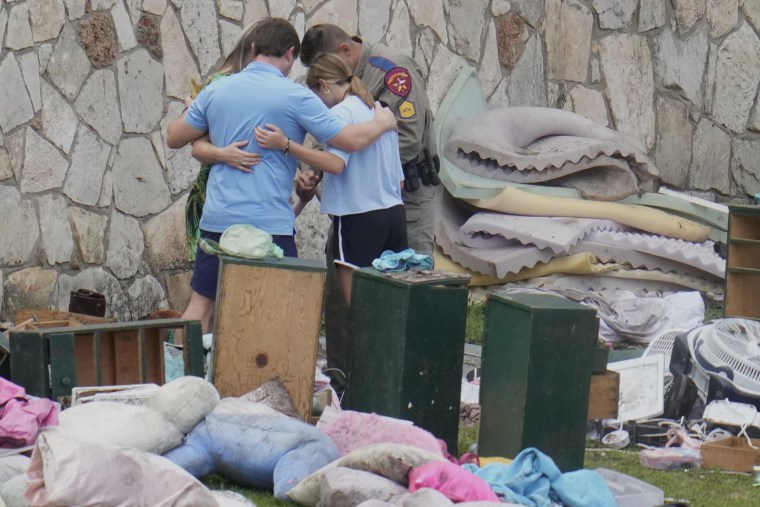 An officer prays with a family as they pick up items at Camp Mystic in Hunt, Texas on Wednesday, July 9, 2025.