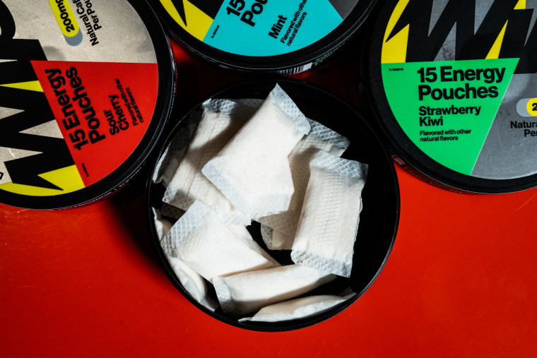 Wip containers displayed on a red table, one of the containers is open and shows white pouches filled with powder inside