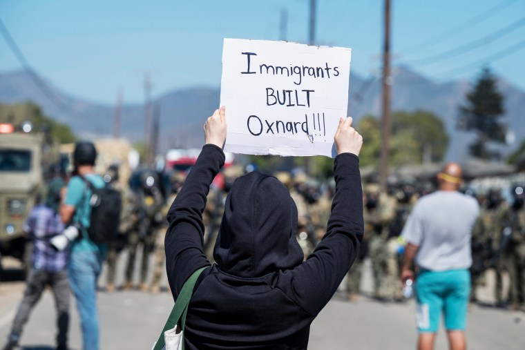 A protester holds a sign that reads, " Immigrants Built Oxnard."