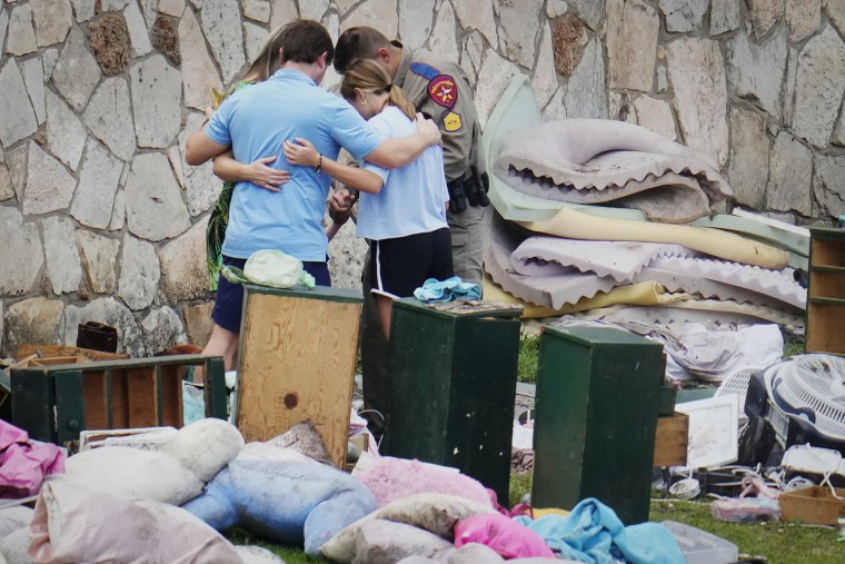 An officer prays with a family as they pick up items at Camp Mystic in Hunt, Texas on Wednesday, July 9, 2025. 
