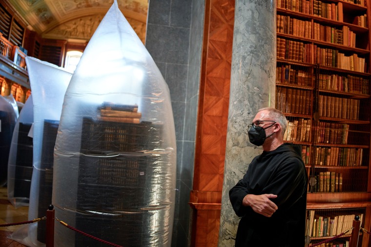 A priest wearing a face mask stands by books kept in hermetically sealed plastic sacks