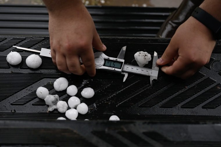 A person holds a measuring tool with a piece of hail.