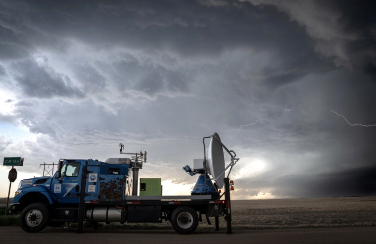 Las tormentas oscuras nubes y un rayo con un camión grande que transporta un satélite y otros equipos en su cama plana.