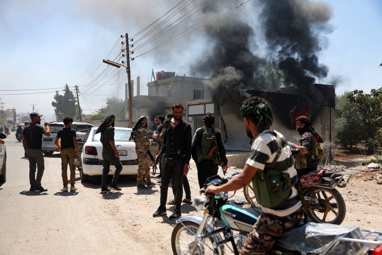 Fighters from Bedouin tribes gather near a burning building in al-Mazraa village, in Syria's southern Sweida governorate, as clashes with Druze gunmen continue on July 18, 2025.