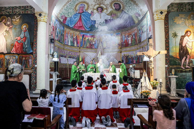 Pierbattista Pizzaballa holds a container with smoke flowing out at the front of the church, people kneel