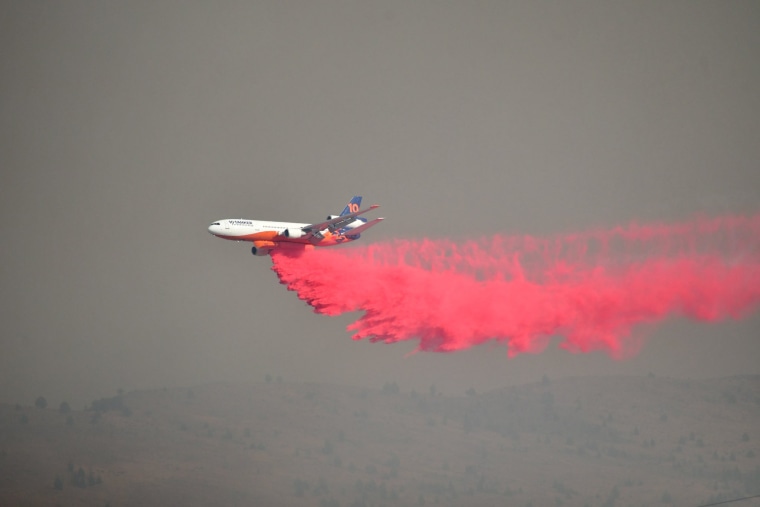 Uma aeronave voa no céu pulverizando fumaça rosa acima da paisagem de fumaça