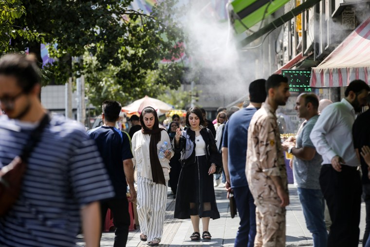 People try to cool off with water sprayed by shops outside