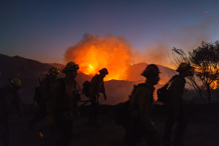 Silhouettes of firefighters seen outside near a blazing fire