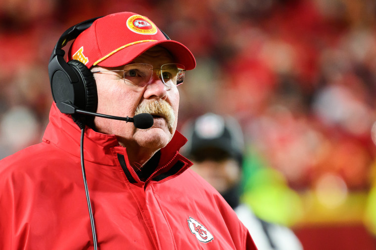 Andy Reid looks on while wearing a headphones and microphone headset on the field