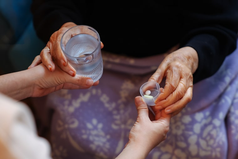 An elderly woman taking a glass of water and pills.